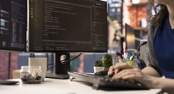 Technician at the office looking at UI on computer monitor and executing programming code. IT freelance worker using coding application to write and test code in modern apartment.