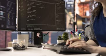 Technician at the office looking at UI on computer monitor and executing programming code. IT freelance worker using coding application to write and test code in modern apartment.